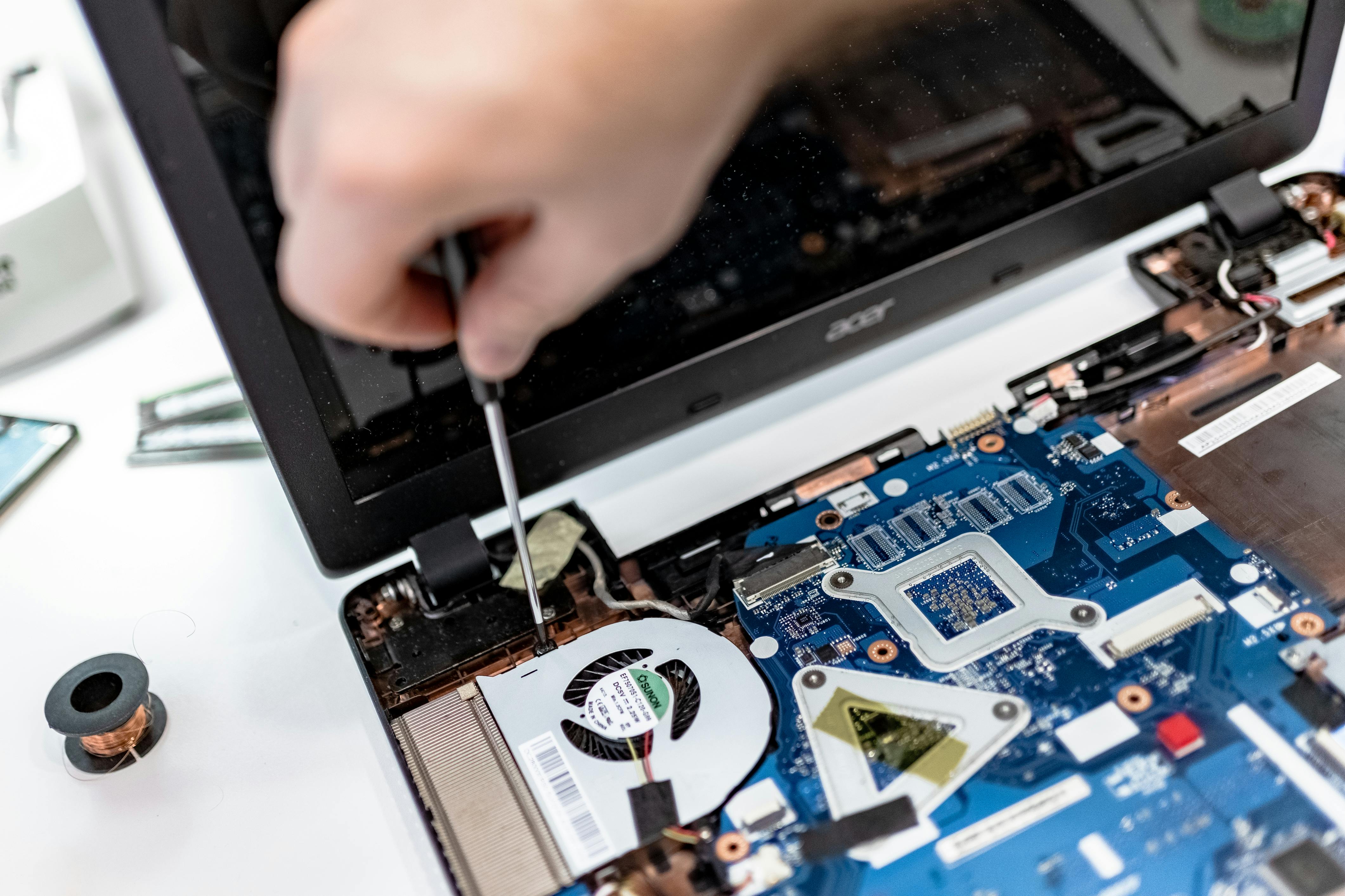 A technician performing a microsurgery on a school laptop by using a screwdriver to tighten internal components, demonstrating proactive preventative maintenance to avoid major hardware failures.