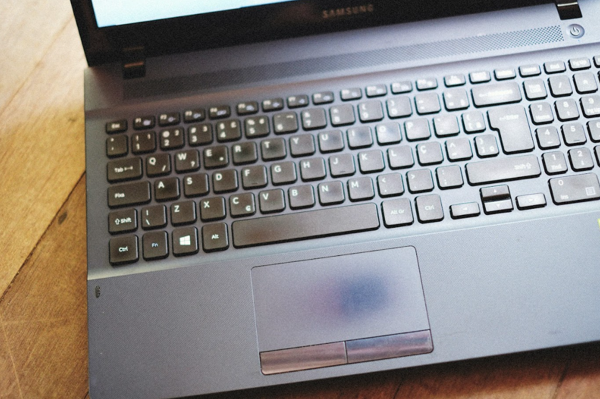 A close-up view of a used laptop keyboard and worn trackpad, illustrating signs of wear that may require school device repair.