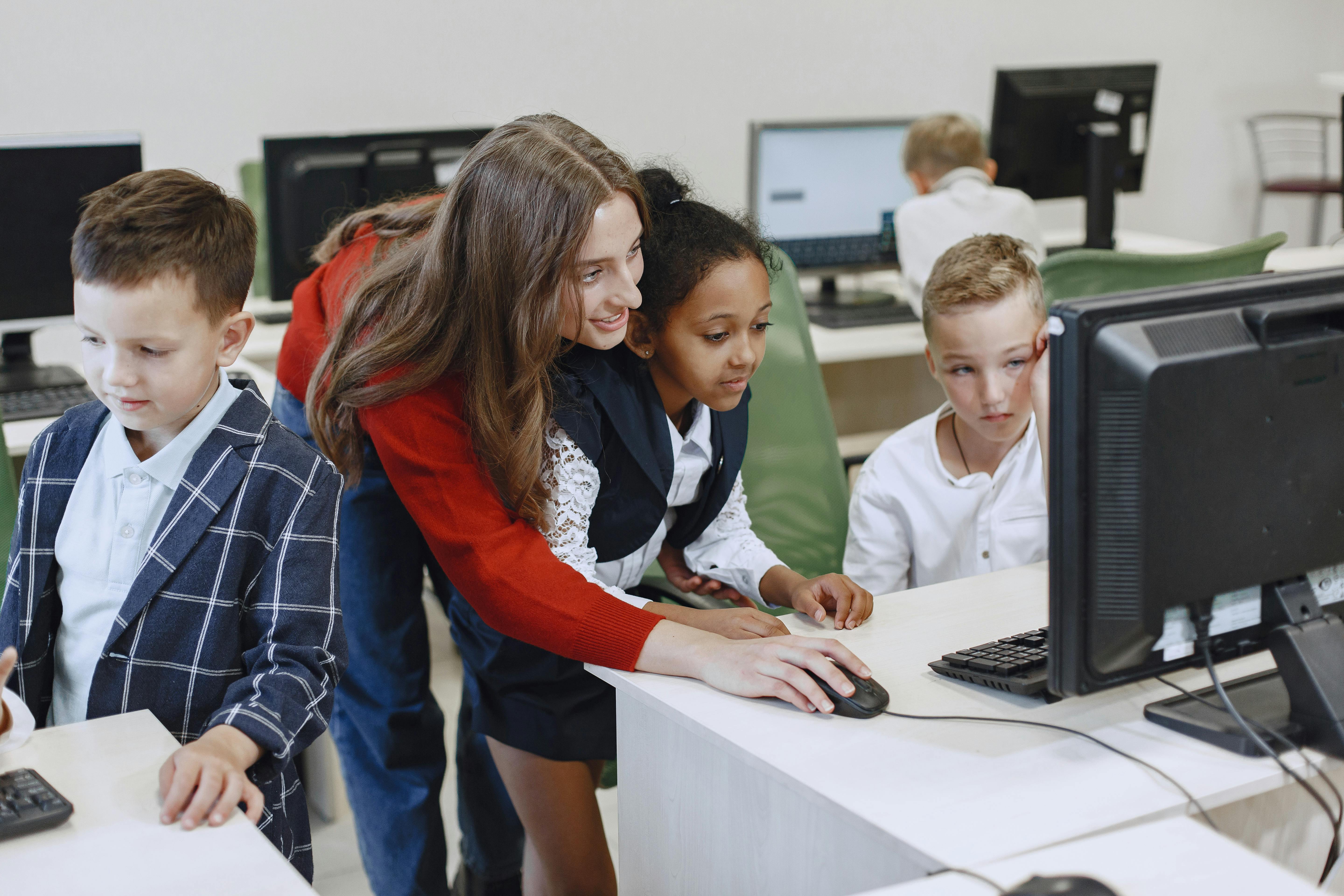 Teacher guiding elementary students as they work together on computers in a school, illustrating hands-on digital learning and the importance of reliable classroom technology.