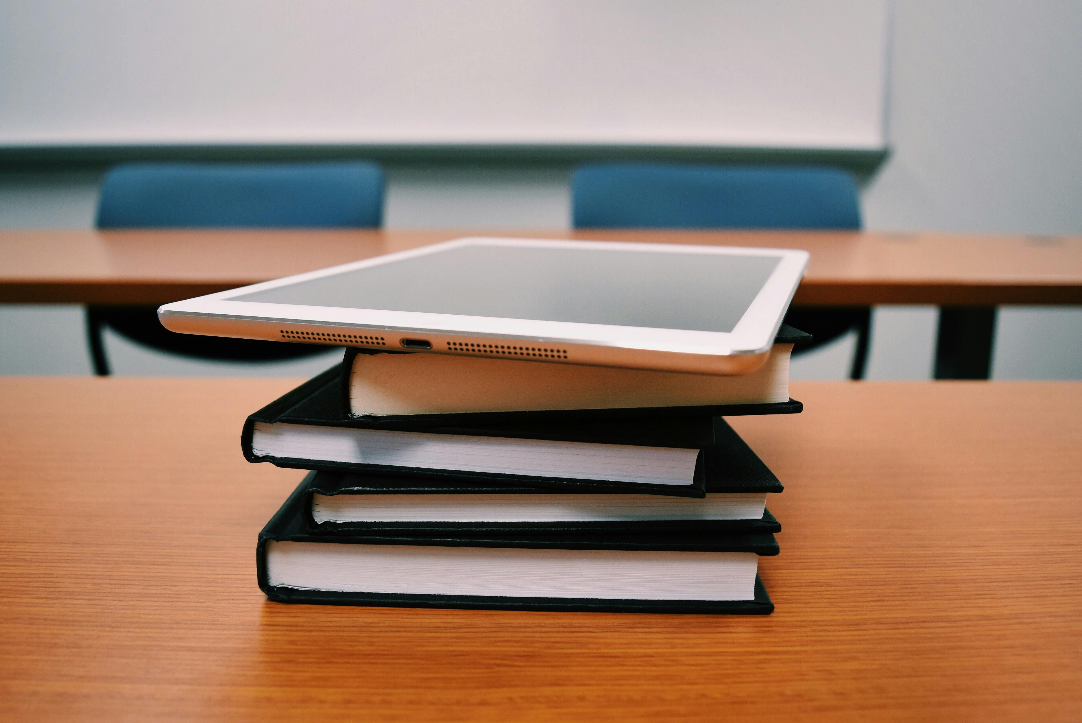 Digital tablet sitting on textbooks, symbolizing the modern classroom's shift to expensive hardware that requires reliable repair coverage.