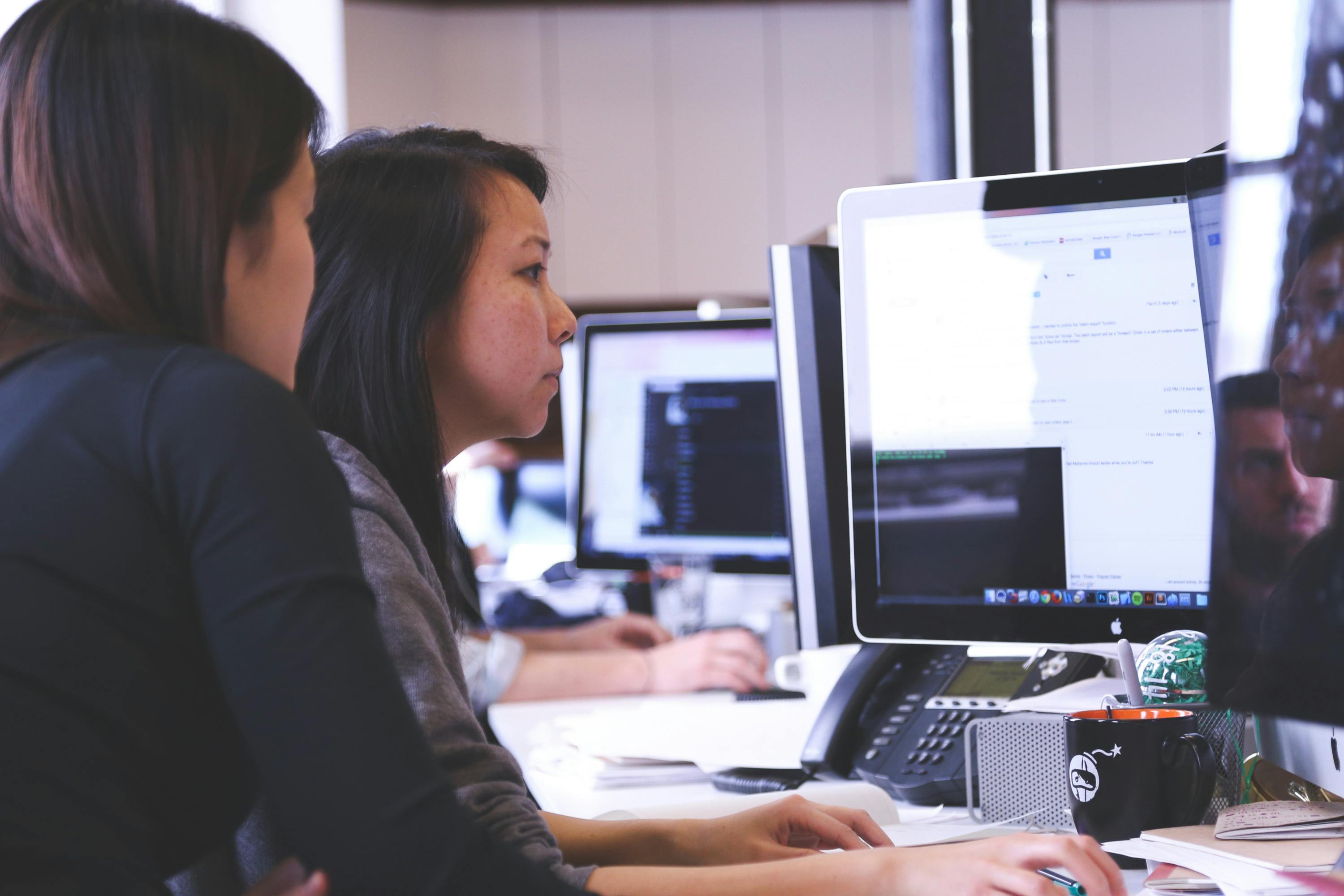 School district IT staff monitoring device repair tracking and diagnostics on computer screens in a technology support office.