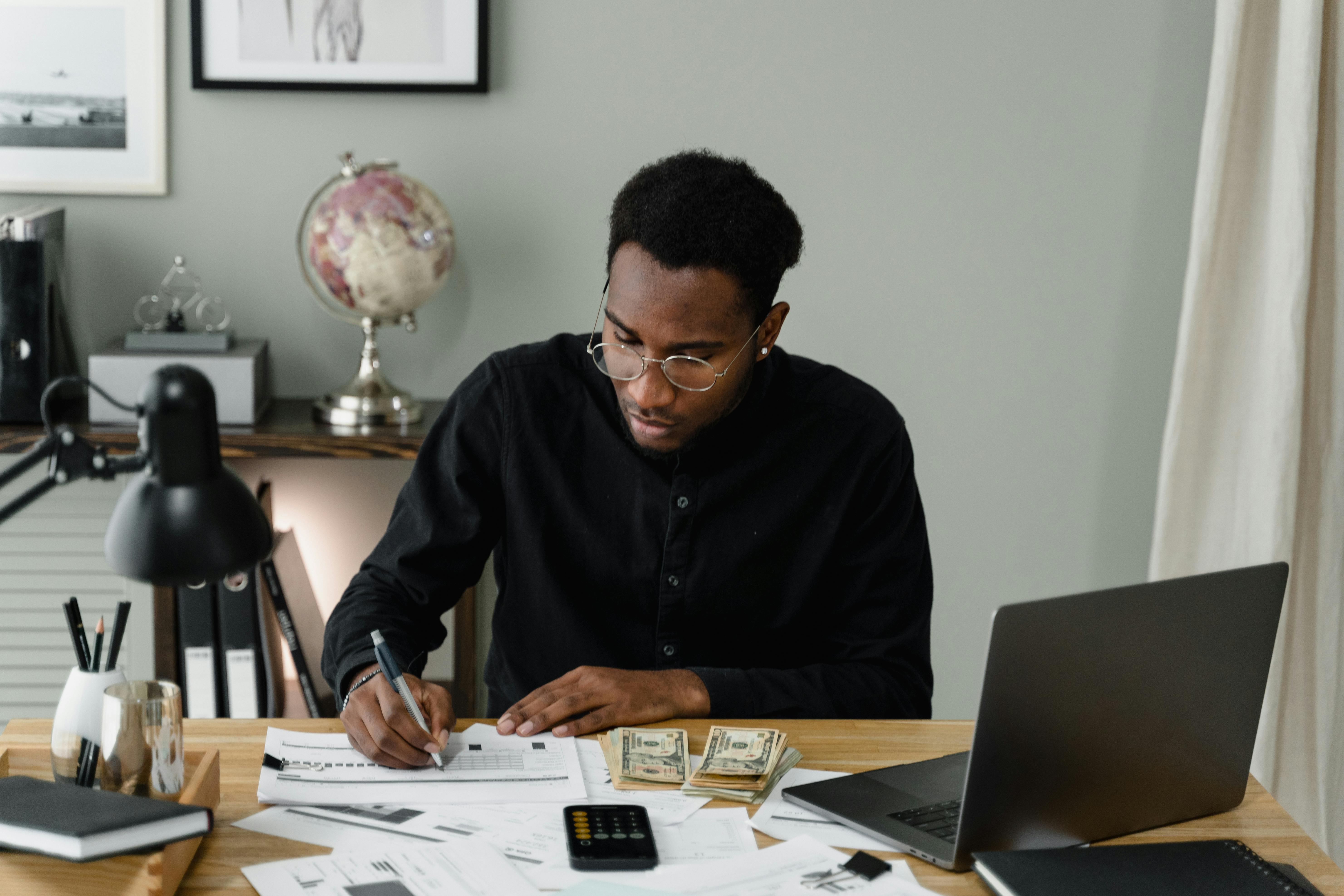 School professional reviewing paperwork and budgeting documents at a desk with a laptop, calculator, and cash, representing strategic planning and cost management for device repairs.